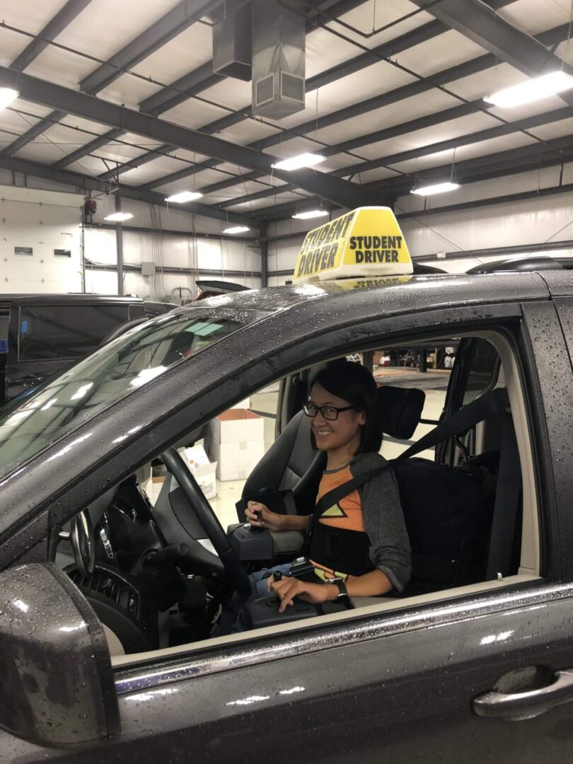 A smiling woman with a gray and orange shirt in a black car
